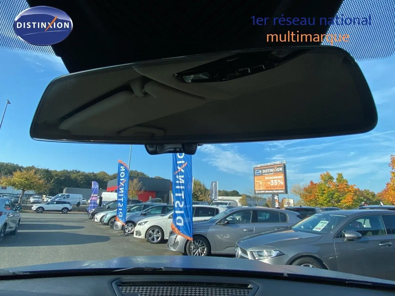 Vue depuis l'intérieur vers l'avant d'un BMW X1 bleu phytonic metal, avec plusieurs voitures en arrière-plan sur un parking.