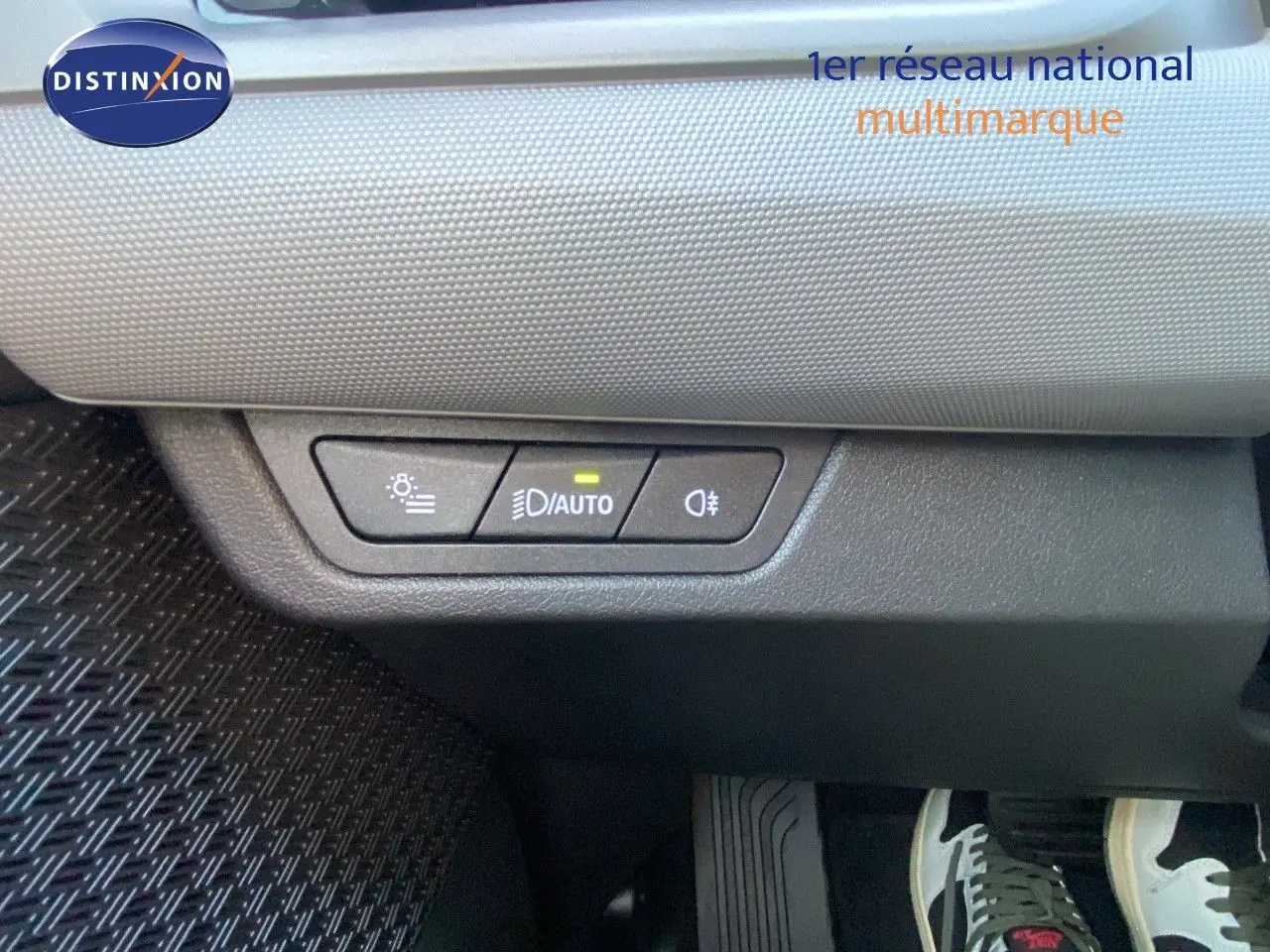 Panneau de commande des phares avec mode automatique allumé, situé sous le tableau de bord d'un BMW X1 bleu phytonic metal.