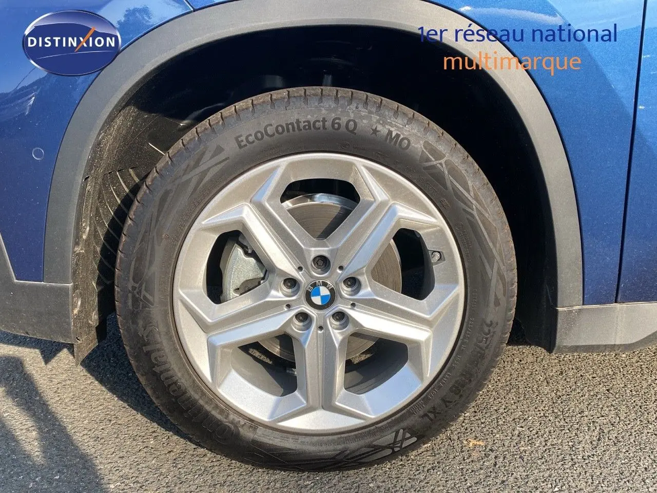 Gros plan sur la roue avant gauche d'un BMW X1 bleu phytonic metal avec jante argentée cinq branches.