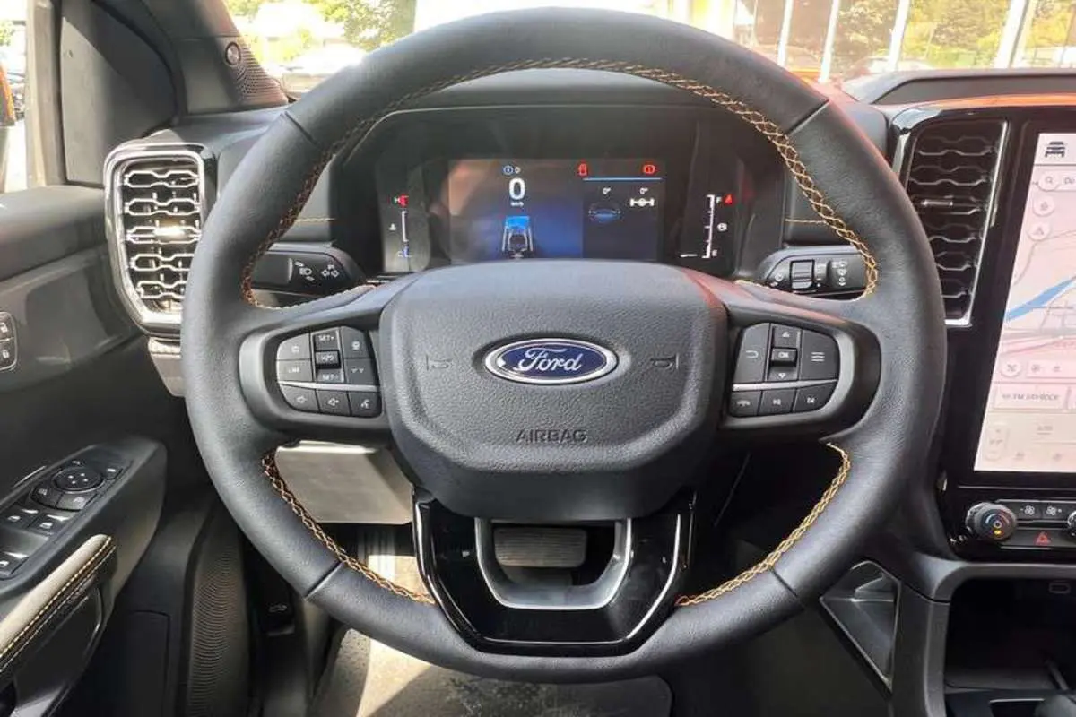 Vue rapprochée du volant en cuir avec surpiqûres marron du Ford Ranger 2025 Wildtrak Plus, tableau de bord numérique visible.
