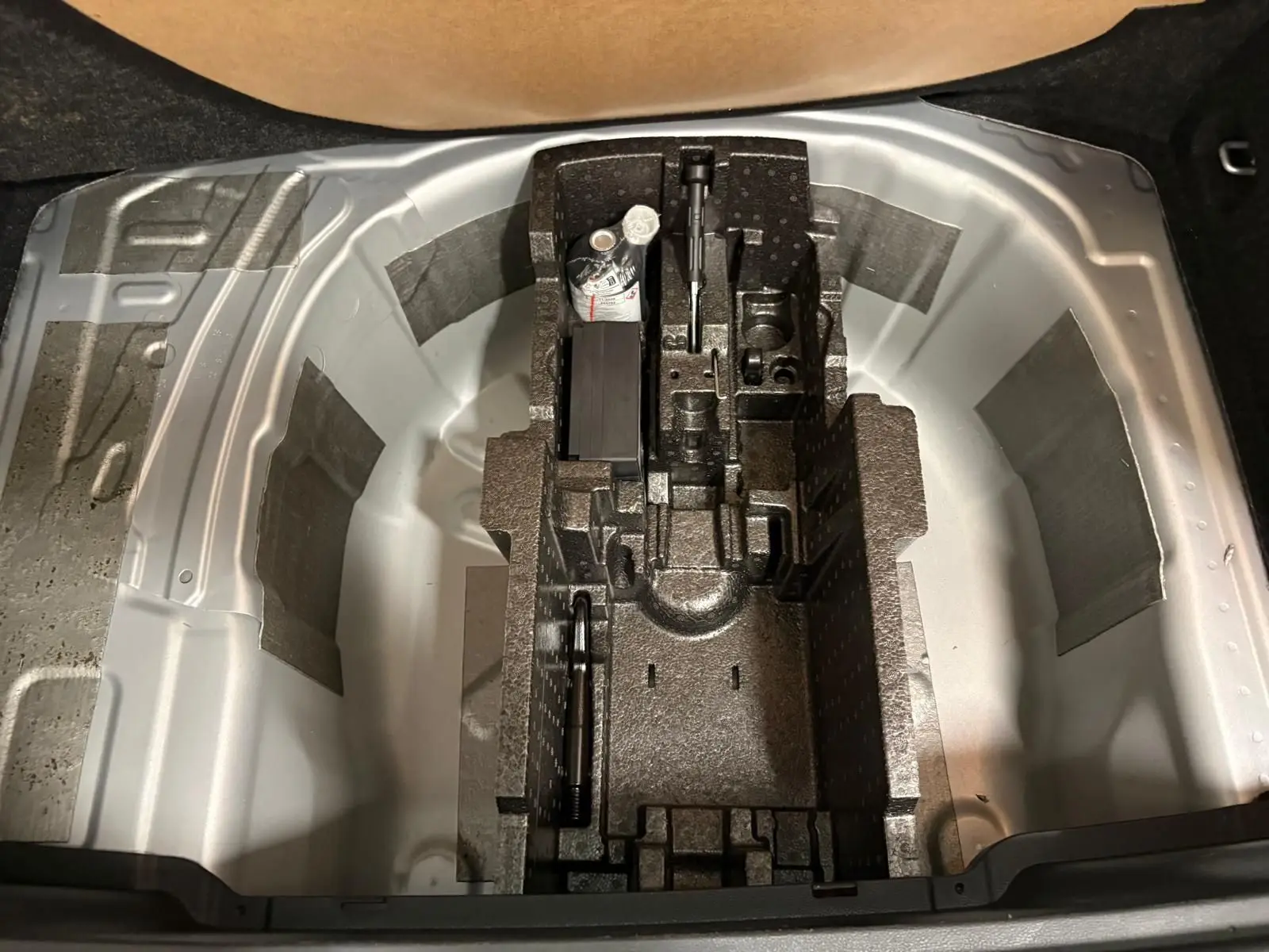 Coffre ouvert du Skoda Kamiq 2025 gris argent, vue plongeante sur le rangement pour roue de secours et outils.