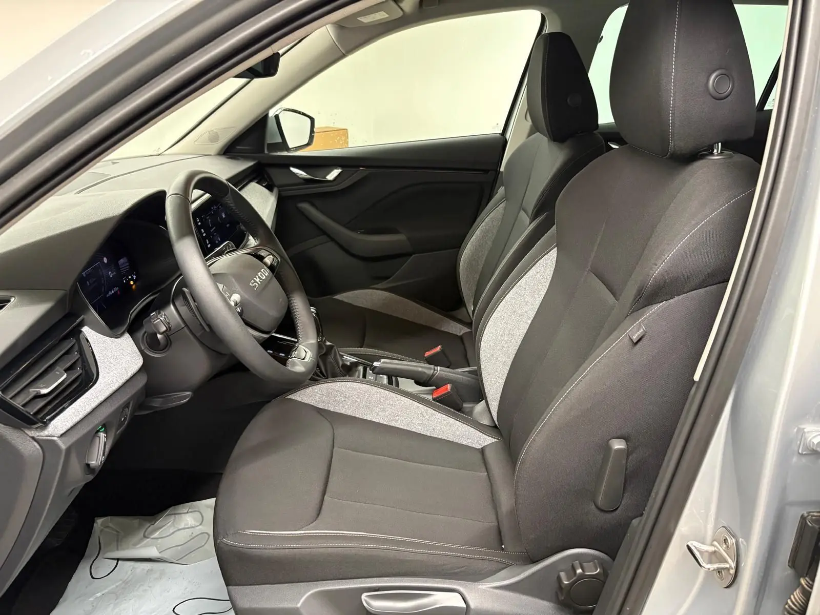 Vue intérieure côté conducteur du Skoda Kamiq gris argent 2025, sièges tissu bicolore noir et gris avec volant multifonction.