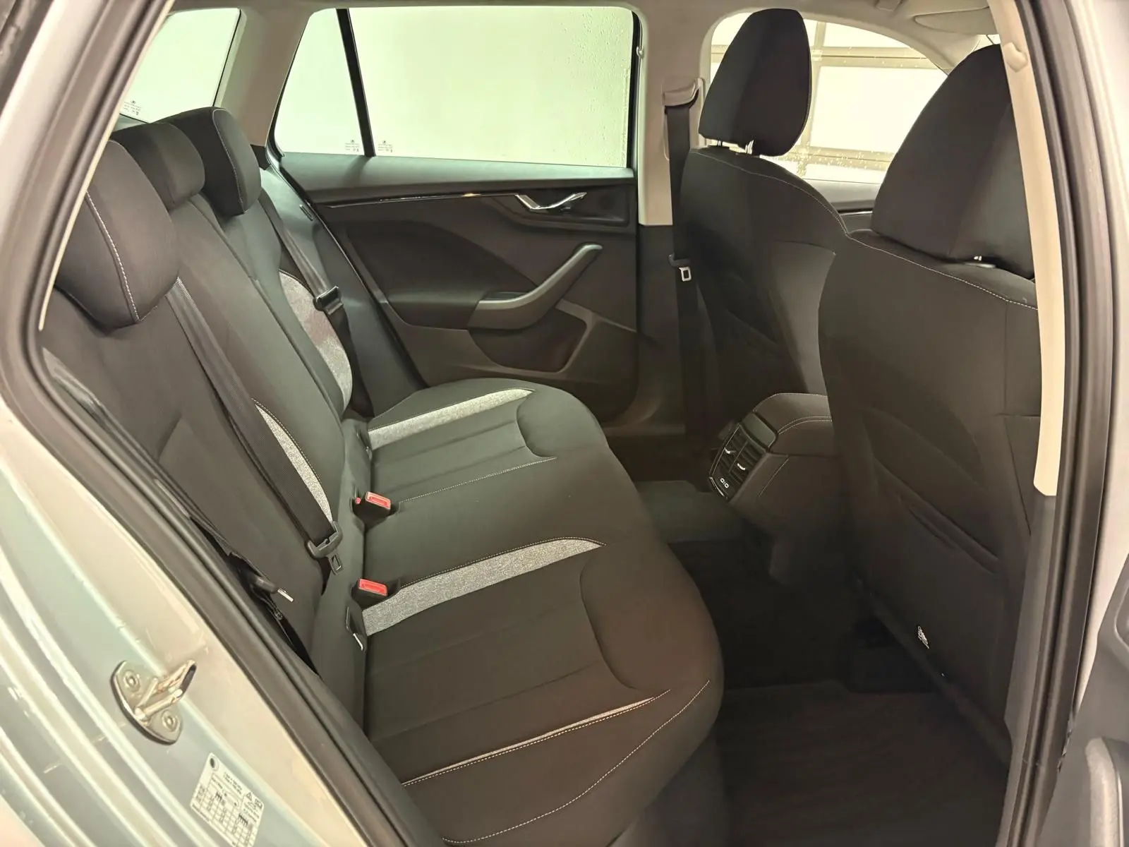 Vue intérieure côté gauche des sièges arrière noirs et gris du Skoda Kamiq gris argent 2025 avec porte ouverte.