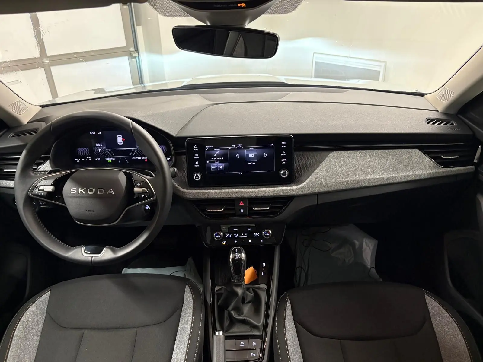 Vue intérieure frontale du tableau de bord et volant noir du Skoda Kamiq 2025 avec écran tactile central et sellerie bicolore.