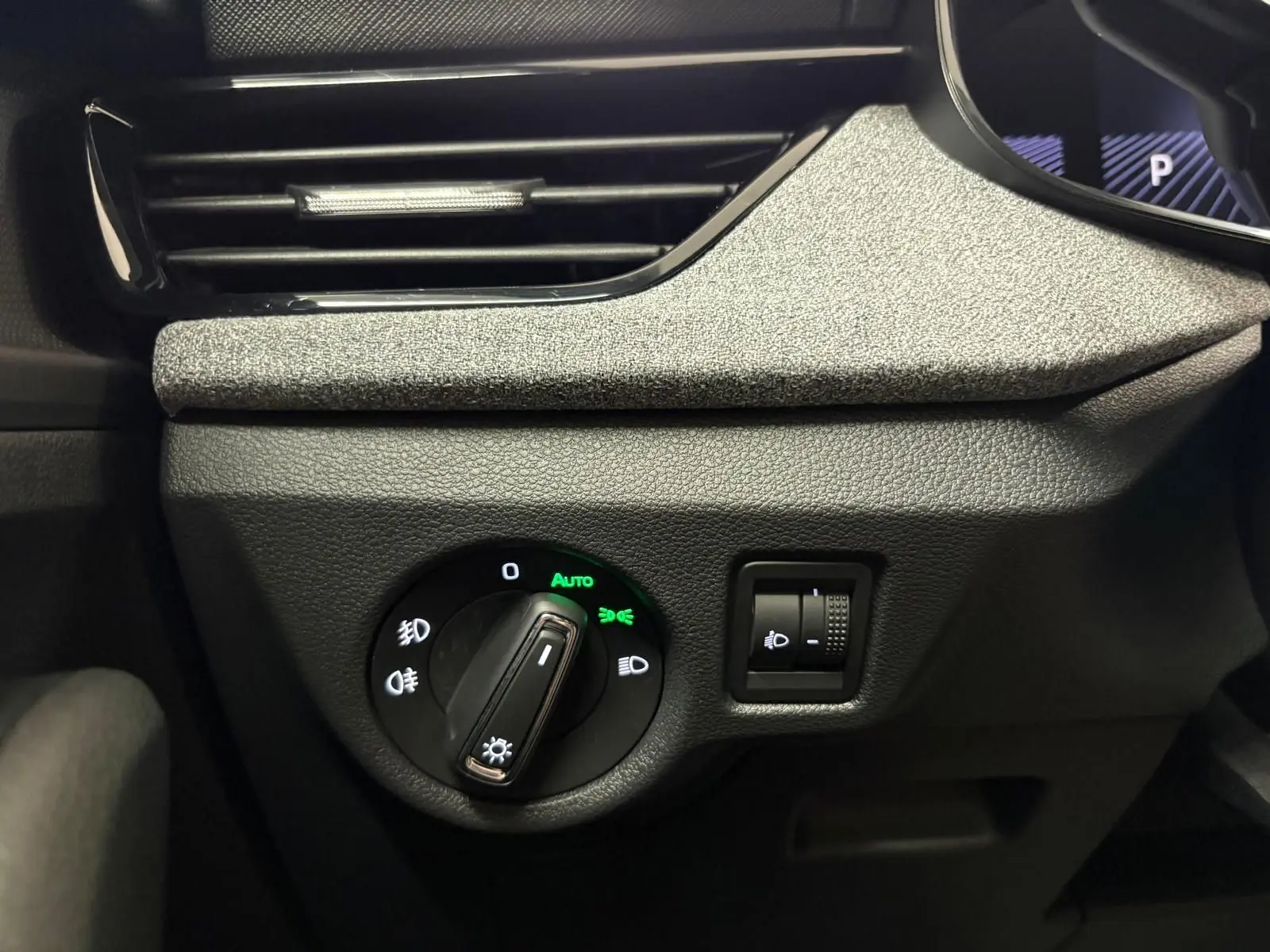 Gros plan sur le bouton de commande des phares du Skoda Kamiq gris argent, avec réglage automatique activé.