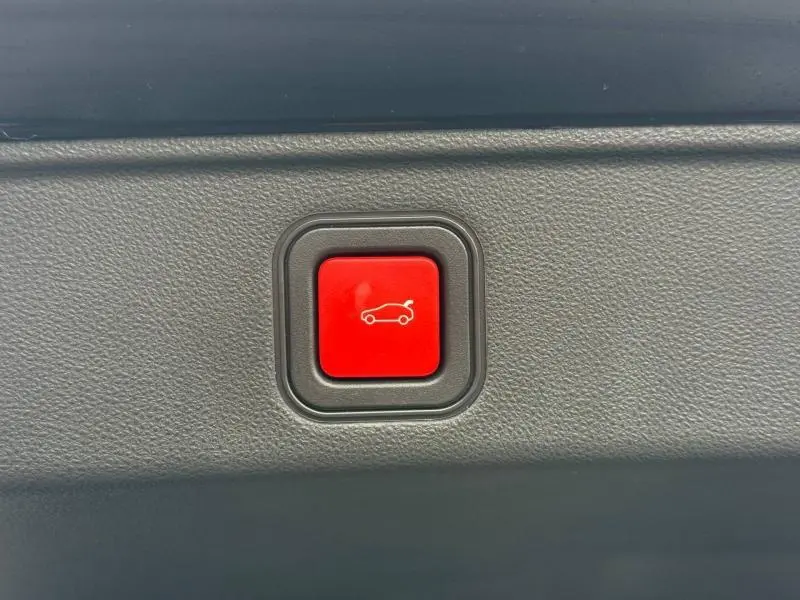 Bouton rouge d'ouverture du coffre sur le panneau intérieur d'une FIAT 600 noire, vue rapprochée.