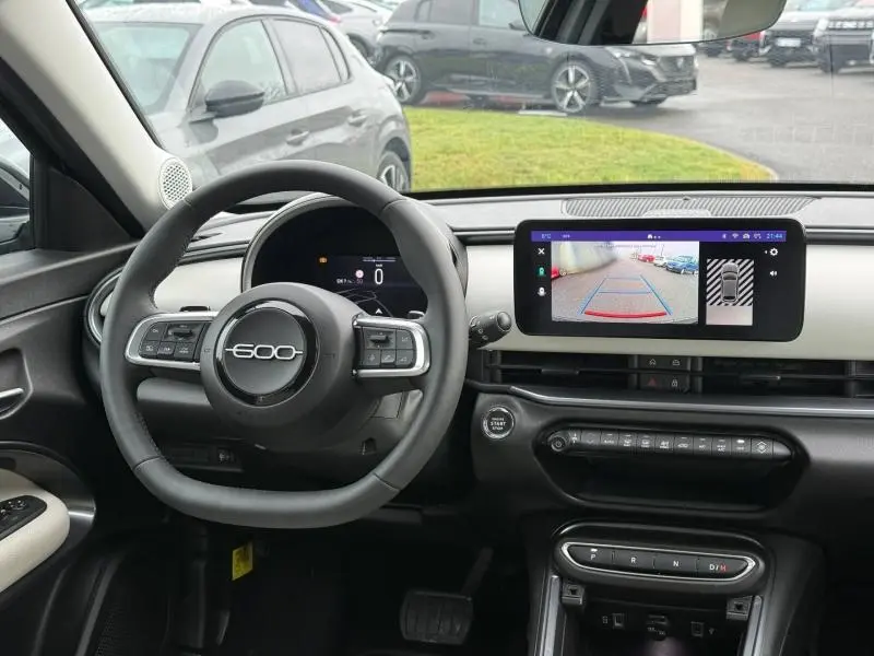 Vue intérieure avant du tableau de bord noir et beige de la FIAT 600 2024 avec écran tactile affichant la caméra de recul.