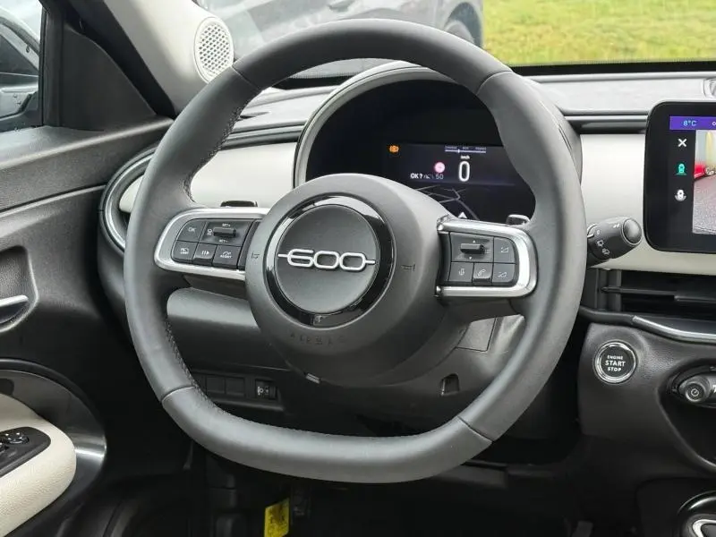 Vue rapprochée du volant noir de la FIAT 600 2024 avec commandes multifonctions et tableau de bord numérique.