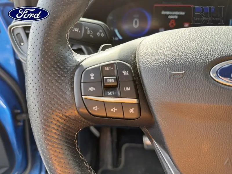Gros plan sur les commandes multifonctions à gauche du volant cuir perforé d’un Ford Puma bleu Fashion Island.
