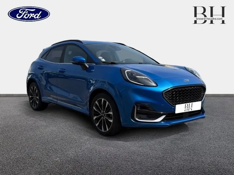 Ford Puma 1.0 EcoBoost bleu métallisé en 3/4 avant droit avec jantes alu et barres de toit noires visibles.