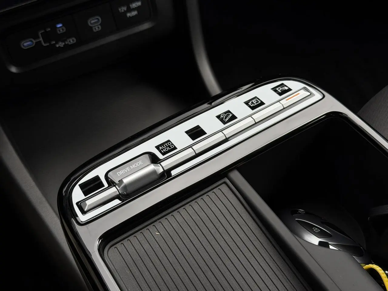 Gros plan sur la console centrale du Hyundai Tucson 2026, boutons argentés et surface noire brillante avec rangement coulissant.