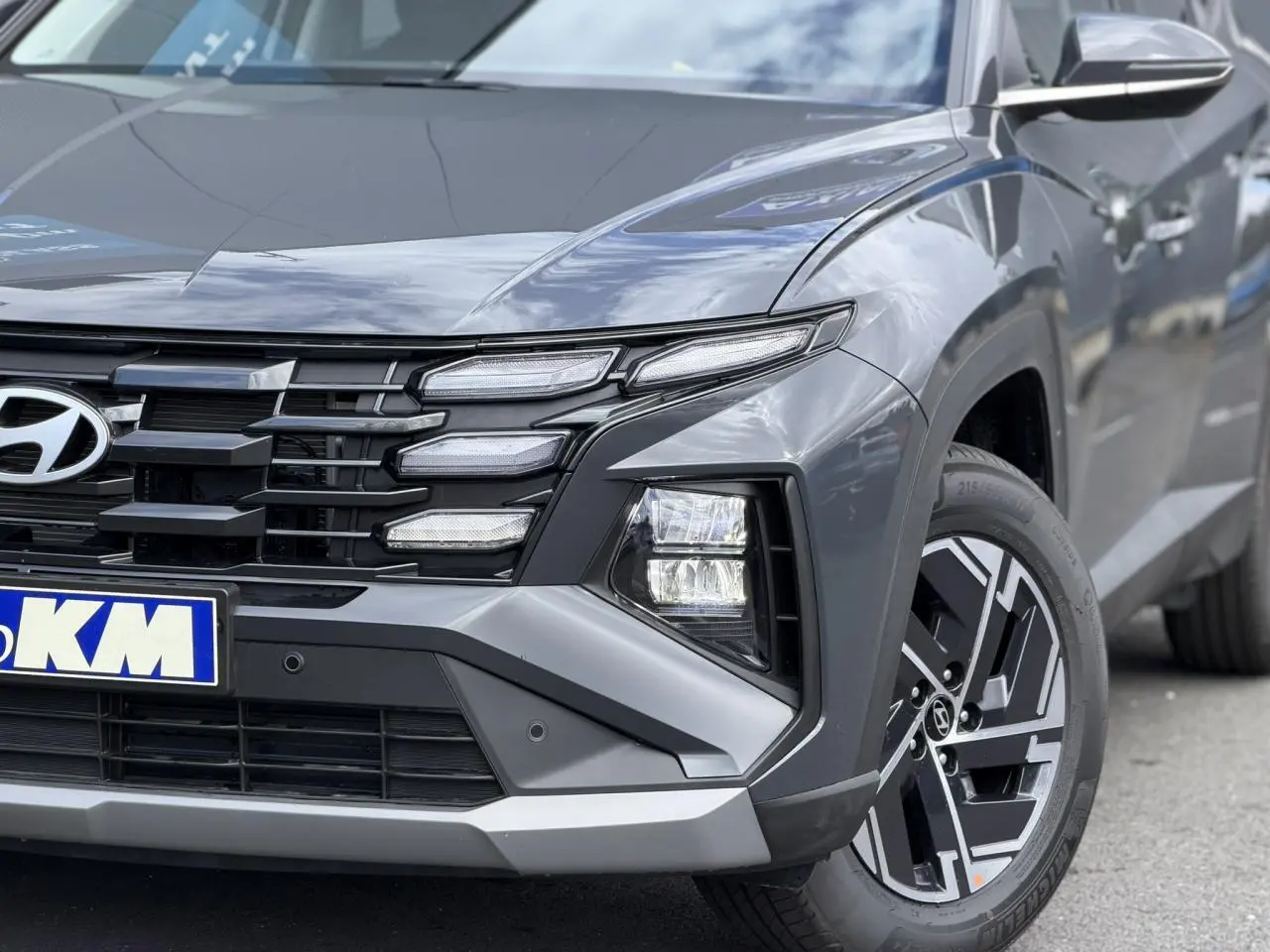 Vue avant droite du Hyundai Tucson 2026 Ecotronic Gray, mettant en valeur la calandre noire et les phares bi-LED distinctifs.
