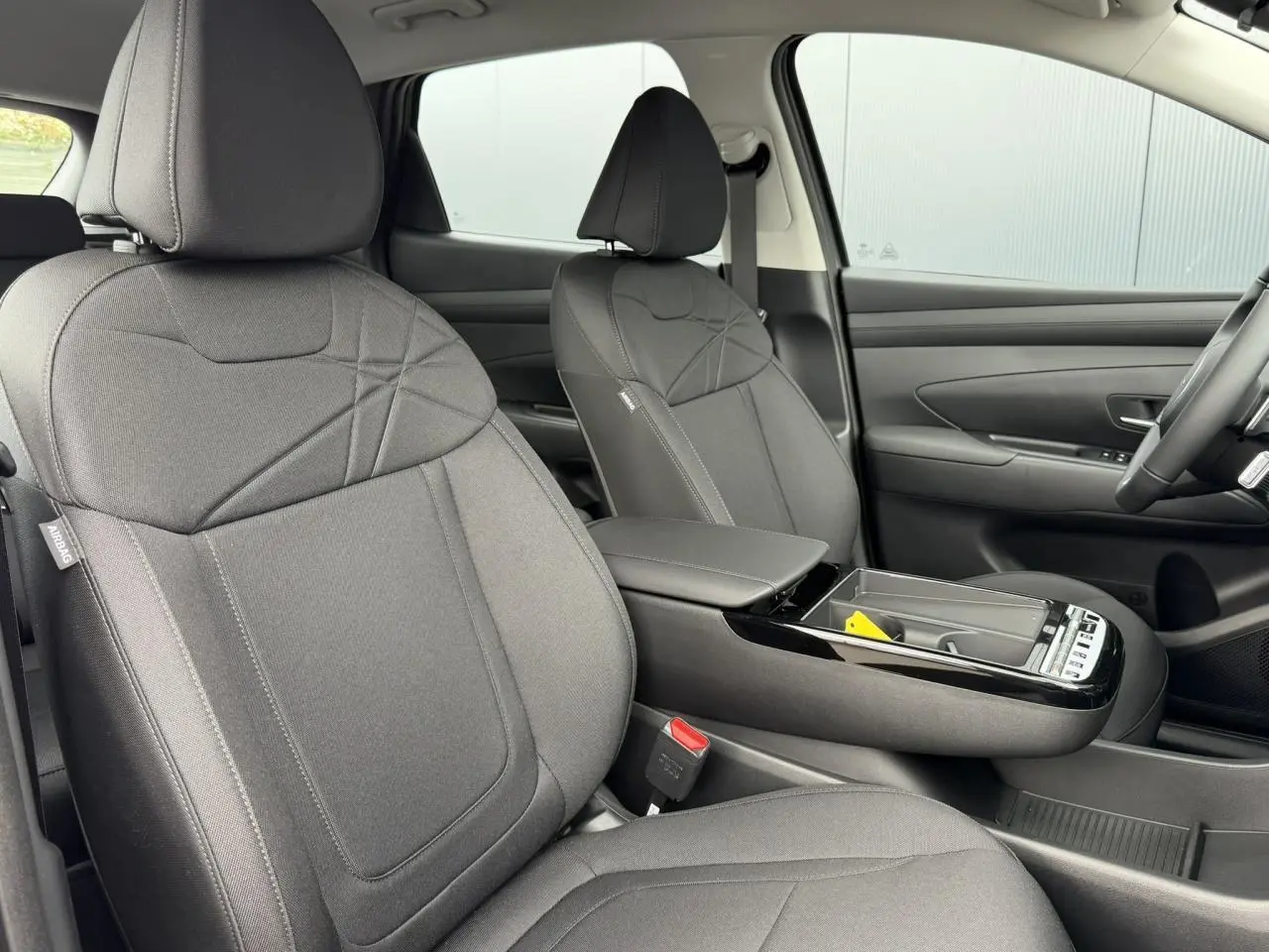 Vue intérieure avant du Hyundai Tucson 2026, sièges tissu gris foncé avec console centrale ouverte et volant visible.