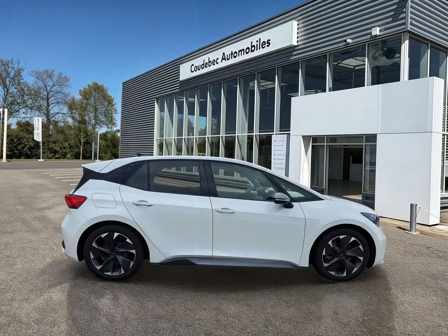 Profil côté gauche de la CUPRA Born électrique blanche 2024 avec jantes alliage noires devant un showroom.