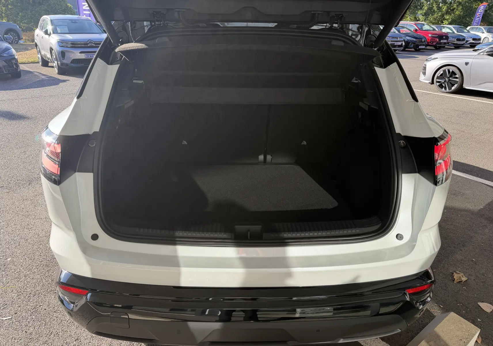 Vue arrière du coffre ouvert du Renault Austral E-Tech 200 Esprit Alpine blanc nacré avec toit noir, en extérieur.