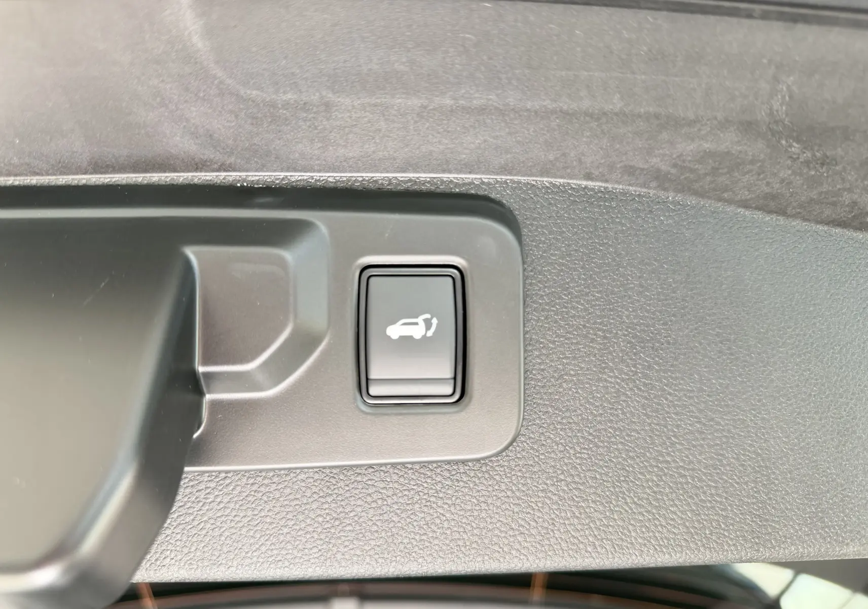 Bouton d'ouverture électrique du hayon sur la garniture intérieure du coffre d'un Renault Austral blanc nacré toit noir.