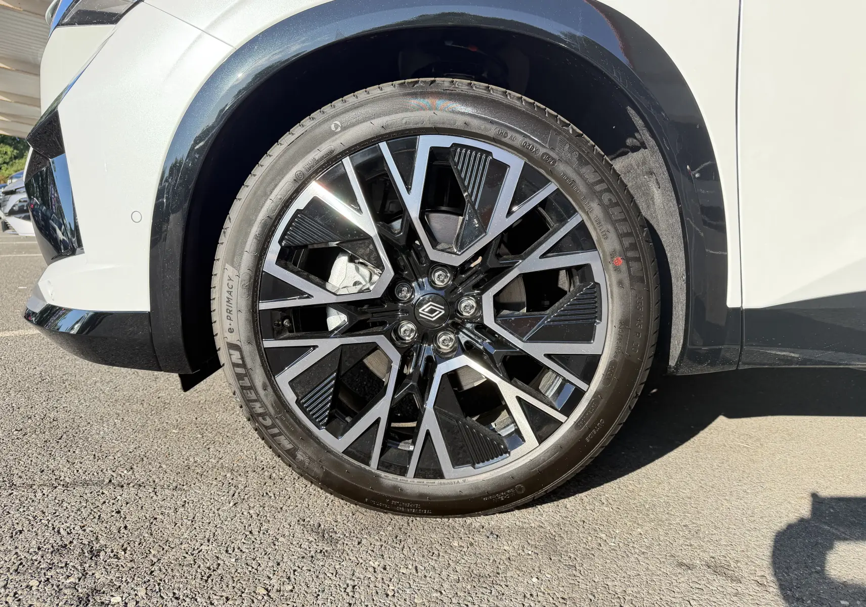 Gros plan sur la jante avant droite noire et argentée du Renault Austral blanc nacré avec passage de roue noir.