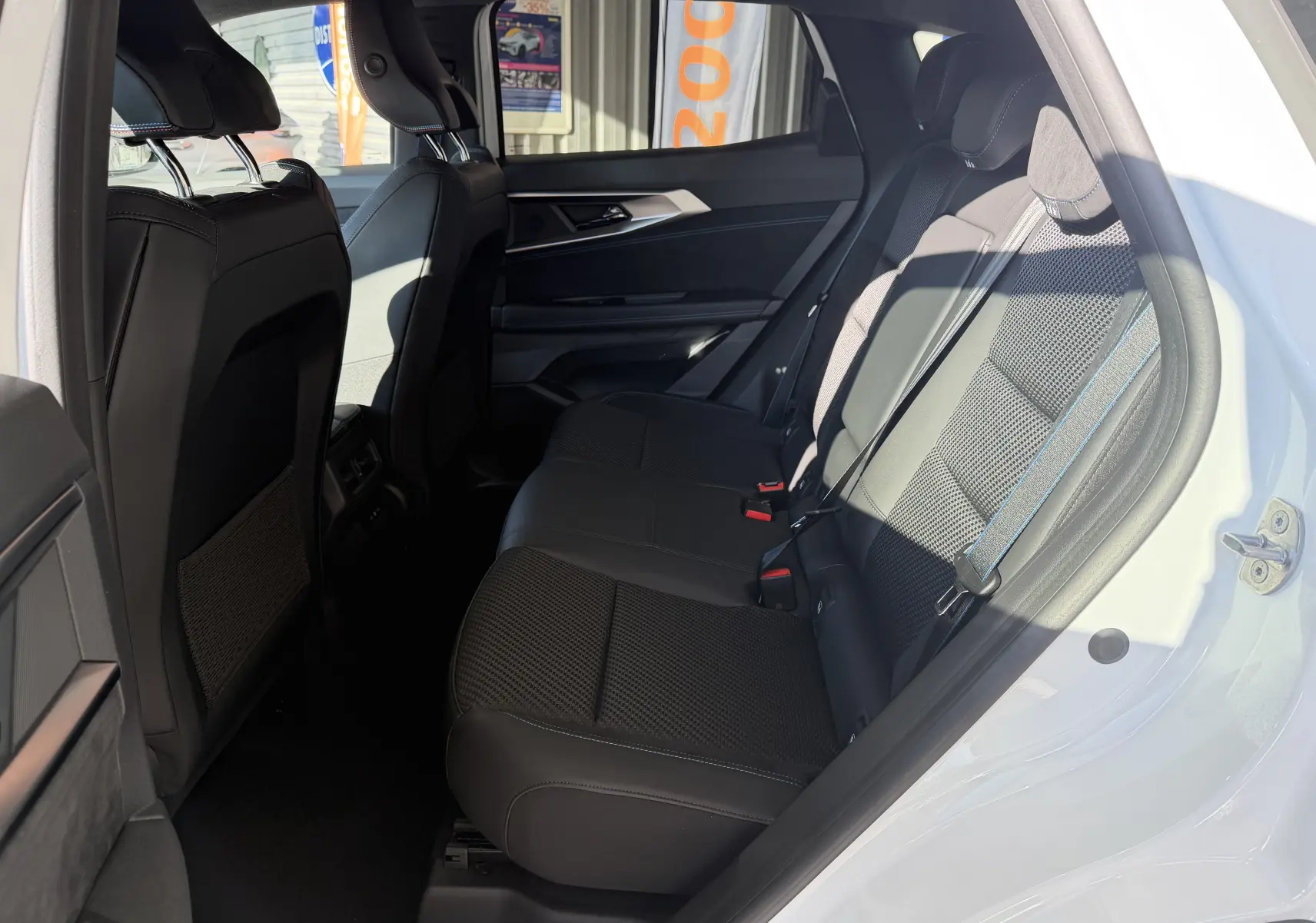Vue latérale droite de l’intérieur arrière du Renault Austral E-Tech 200 Esprit Alpine, sièges noirs avec surpiqûres bleues.