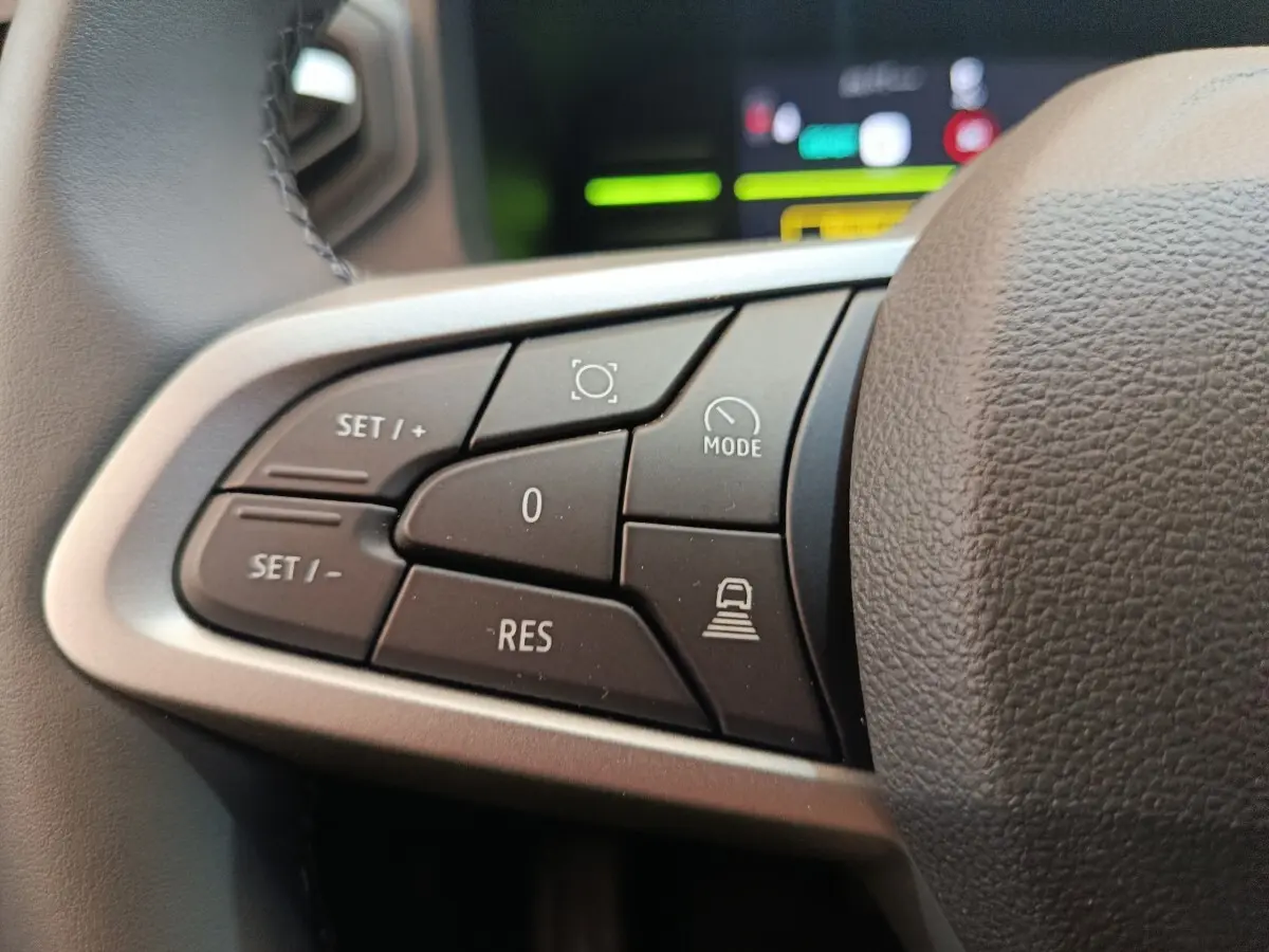 Gros plan sur les commandes au volant du Dacia Duster Journey Hybrid 155, boutons noirs avec marquages blancs.