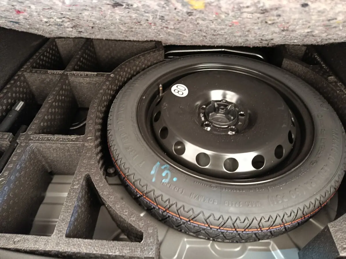 Roue de secours noire dans le coffre compartimenté d'un Dacia Duster noir, vue en plongée rapprochée.