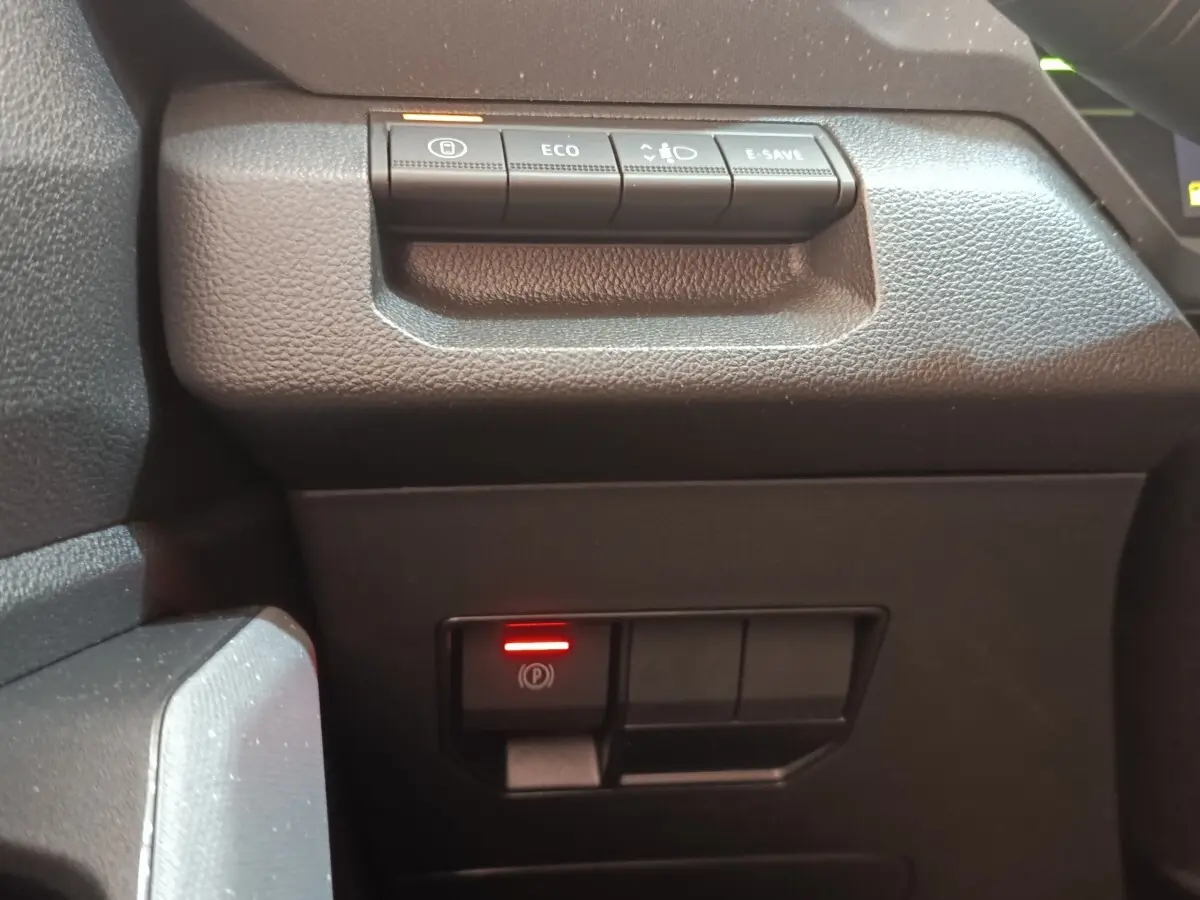 Gros plan sur les commandes noires du tableau de bord du Dacia Duster Journey Hybrid 155, avec bouton frein à main électrique allumé.