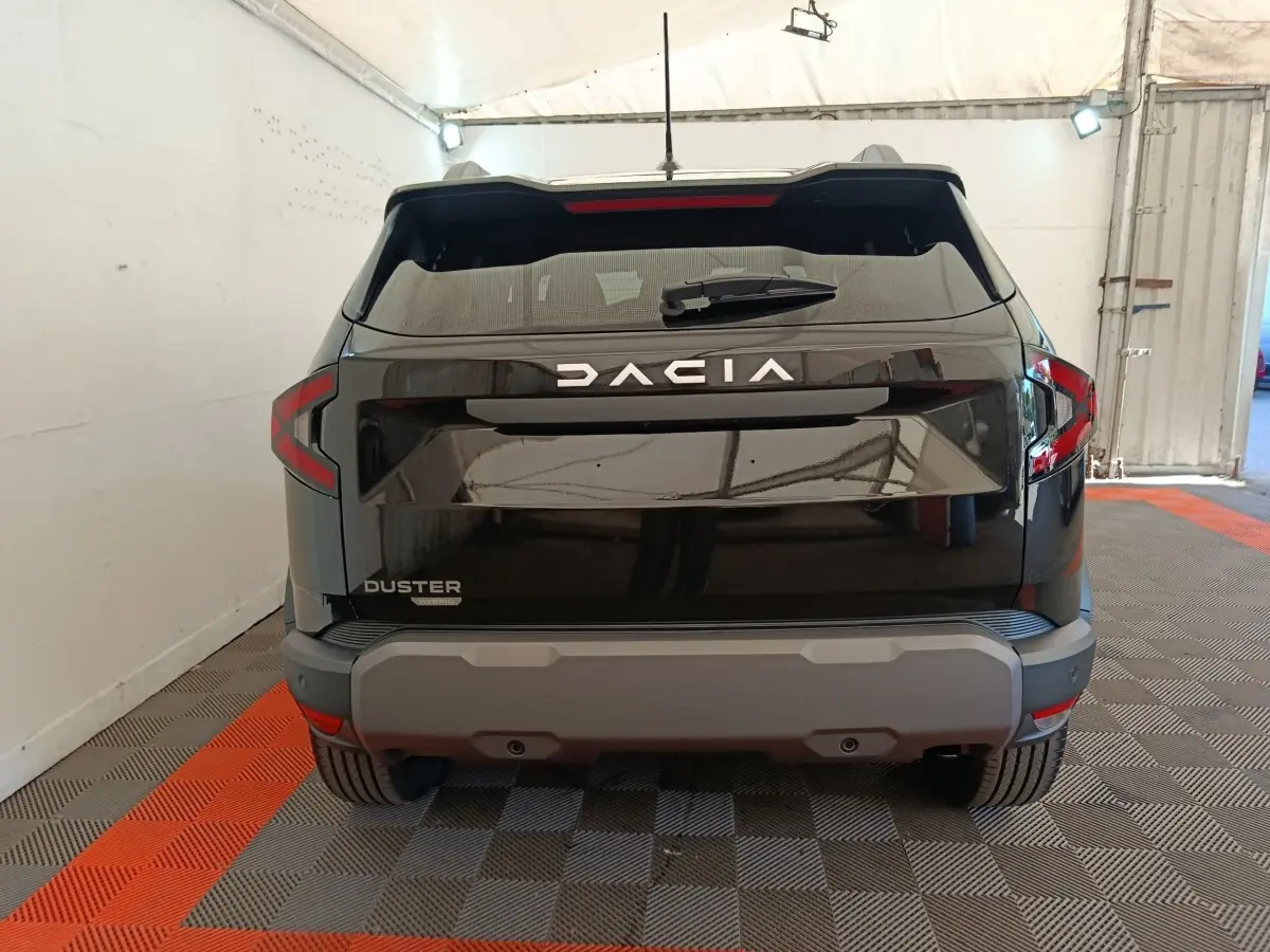 Vue arrière du Dacia Duster noir 2026 avec logo DACIA lumineux et pare-chocs gris dans un garage.