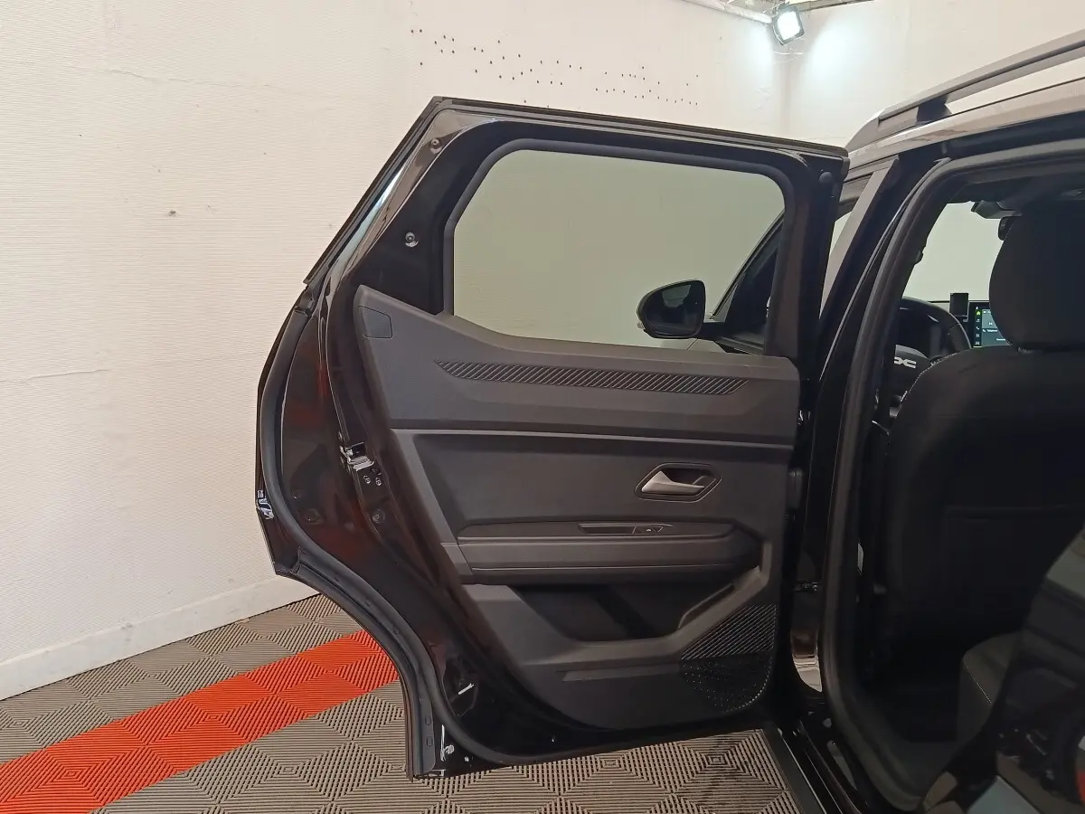 Vue intérieure de la porte arrière droite ouverte d'un Dacia Duster Journey Hybrid 155 noir, montrant les détails de la garniture.