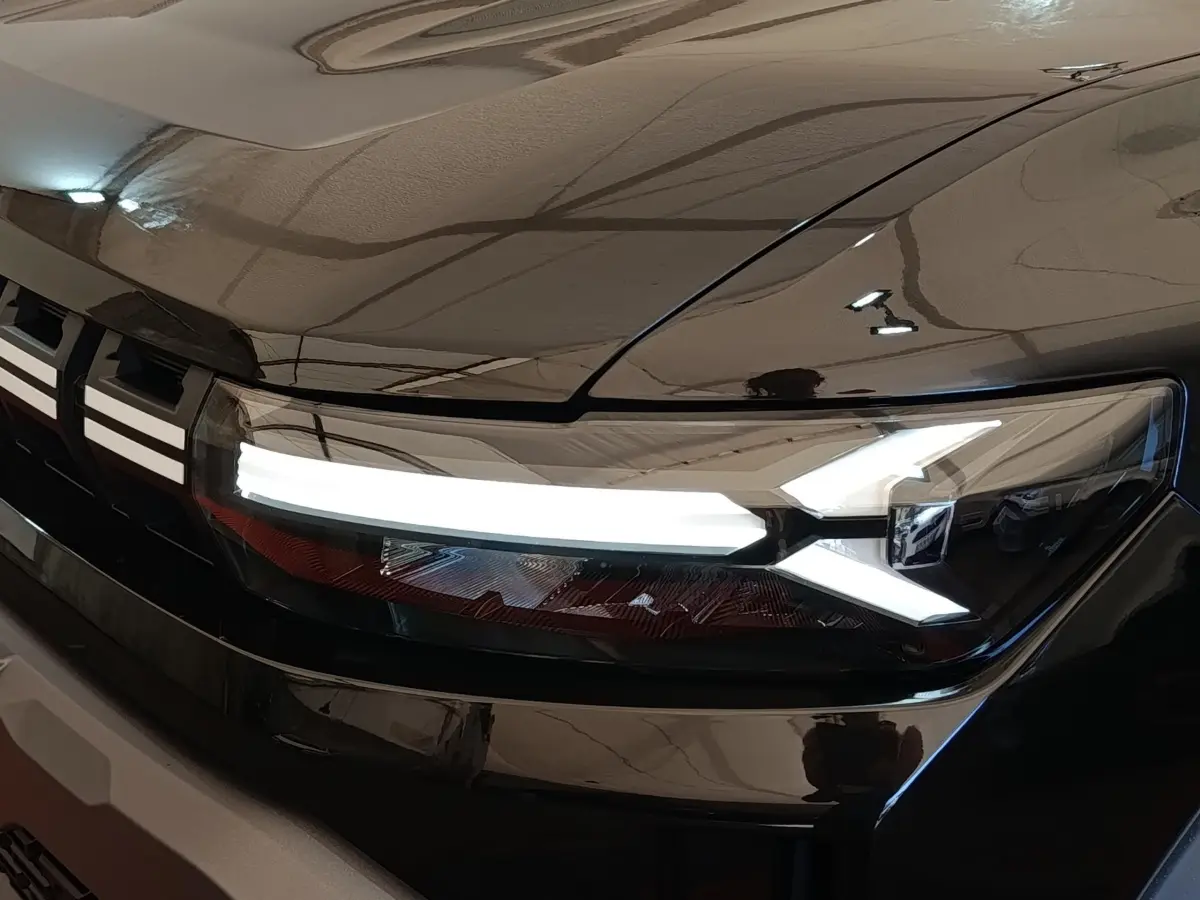 Gros plan sur le phare avant droit allumé du Dacia Duster Journey Hybrid 155 noir, soulignant ses lignes LED distinctives.