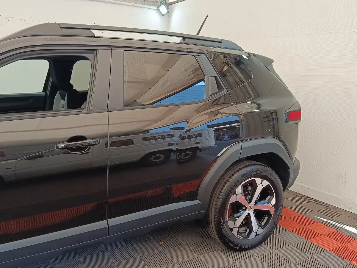 Vue latérale droite du Dacia Duster Journey Hybrid 155 noir, mettant en valeur la roue arrière et les rails de toit noirs.