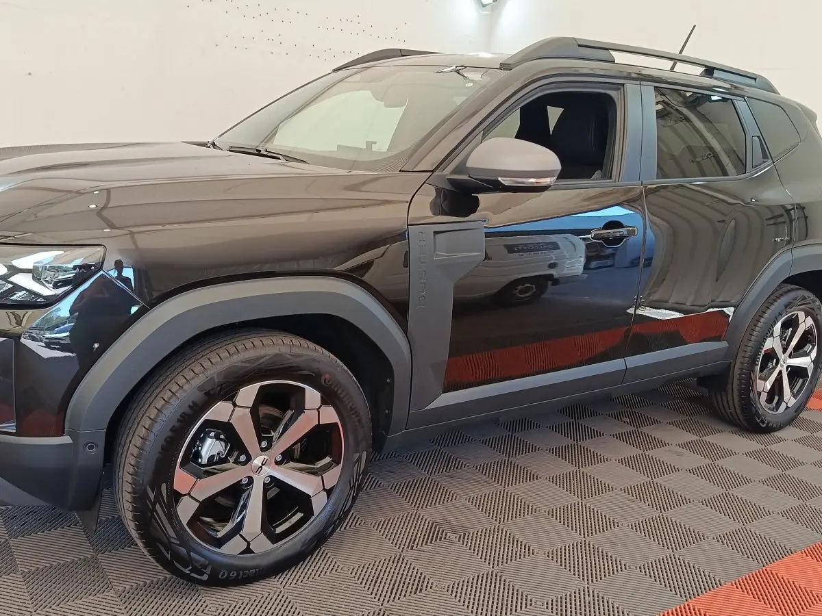 Vue de profil côté gauche du Dacia Duster Journey Hybrid 155 noir, avec jantes alliage et barres de toit noires.