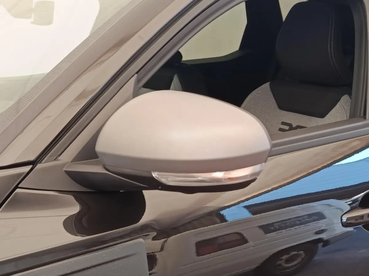 Gros plan sur le rétroviseur côté gauche d'un Dacia Duster Journey Hybrid 155 noir avec siège avant visible.