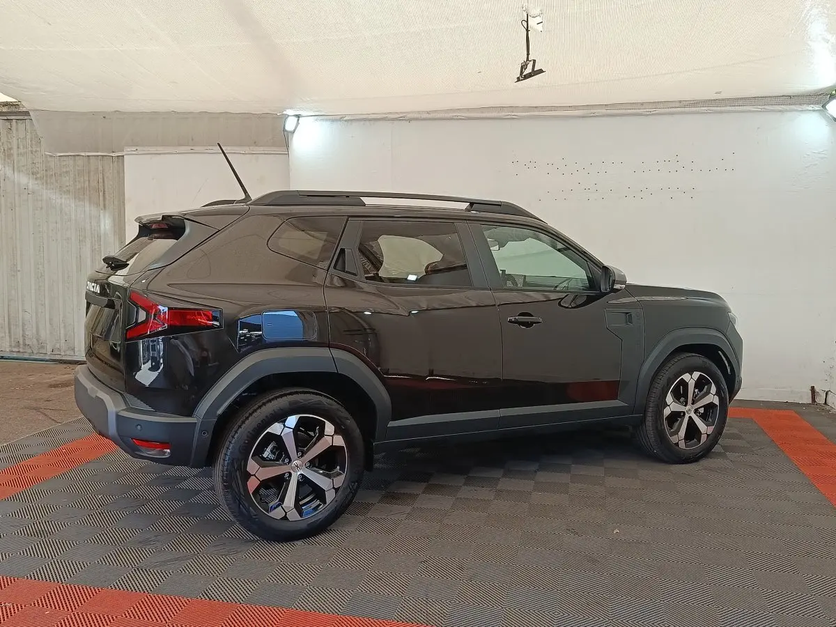Vue de profil côté gauche d'un Dacia Duster Journey Hybrid 155 noir, avec jantes alliage et barres de toit noires.