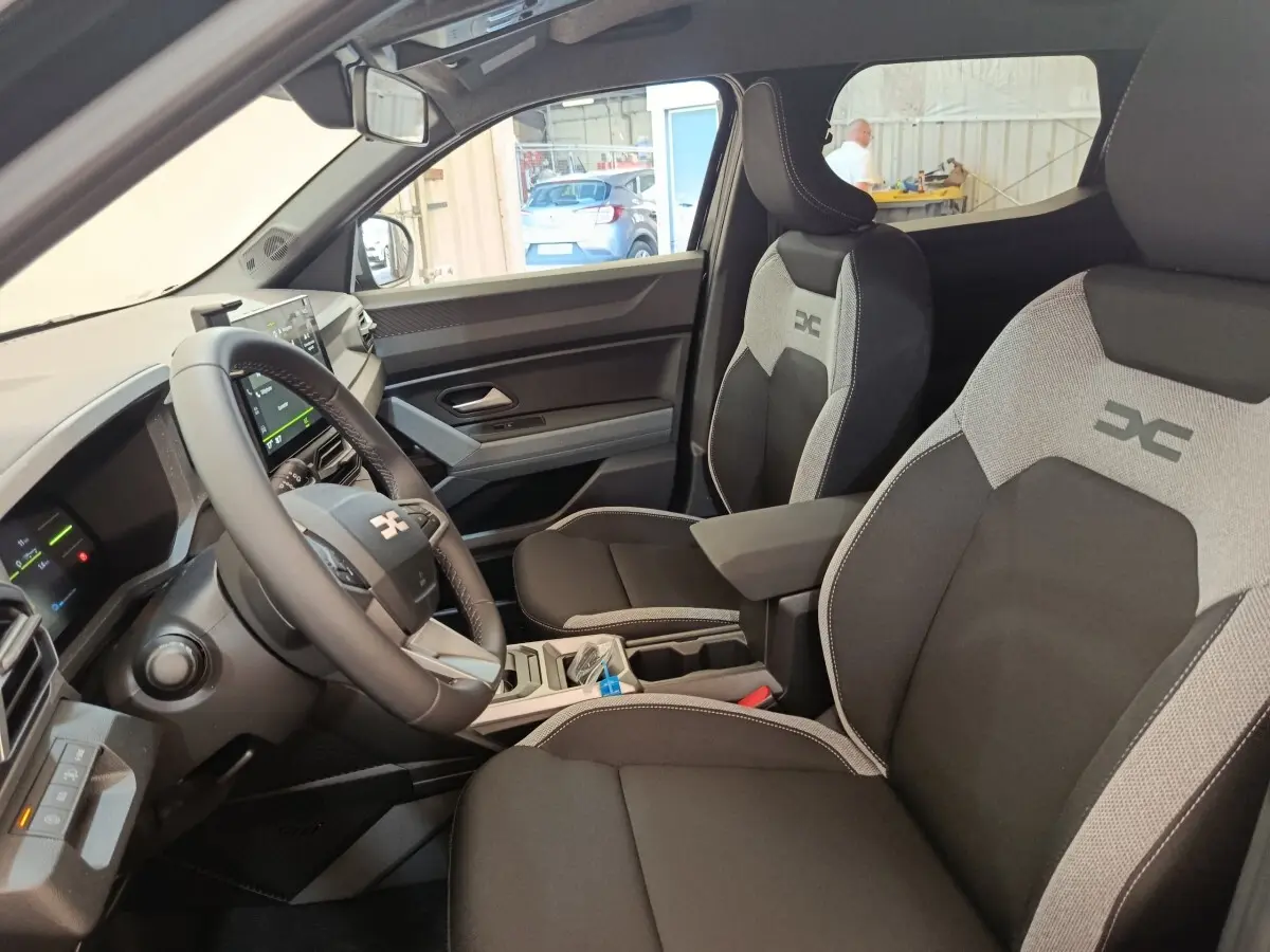 Vue intérieure côté conducteur du Dacia Duster Journey Hybrid 155 avec sièges noirs et gris et volant multifonctions.
