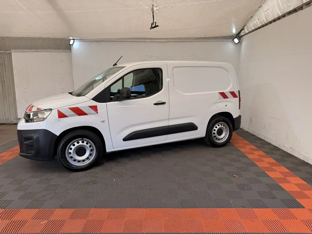 Vue de profil côté gauche d’un Citroën Berlingo blanc 2019 avec bandes rouges diagonales sur l’aile avant et l’arrière.