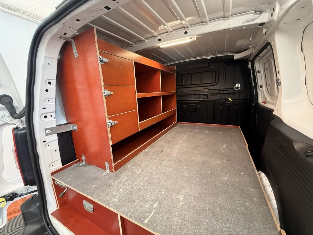 Vue intérieure arrière du Citroën Berlingo blanc 2019, montrant l'aménagement bois avec étagères et rangements.