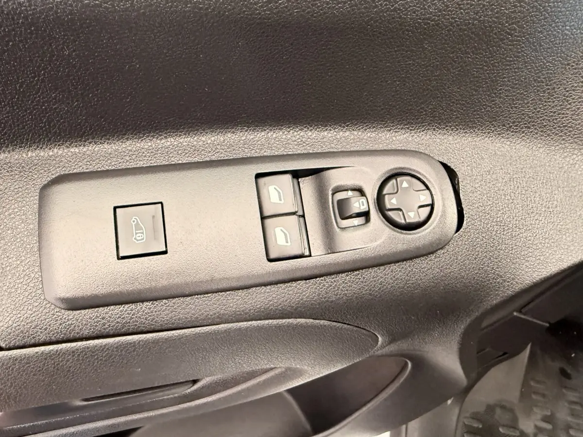Détail des commandes de réglage des vitres et des rétroviseurs sur la porte côté conducteur d’un Citroën Berlingo blanc de 2019.