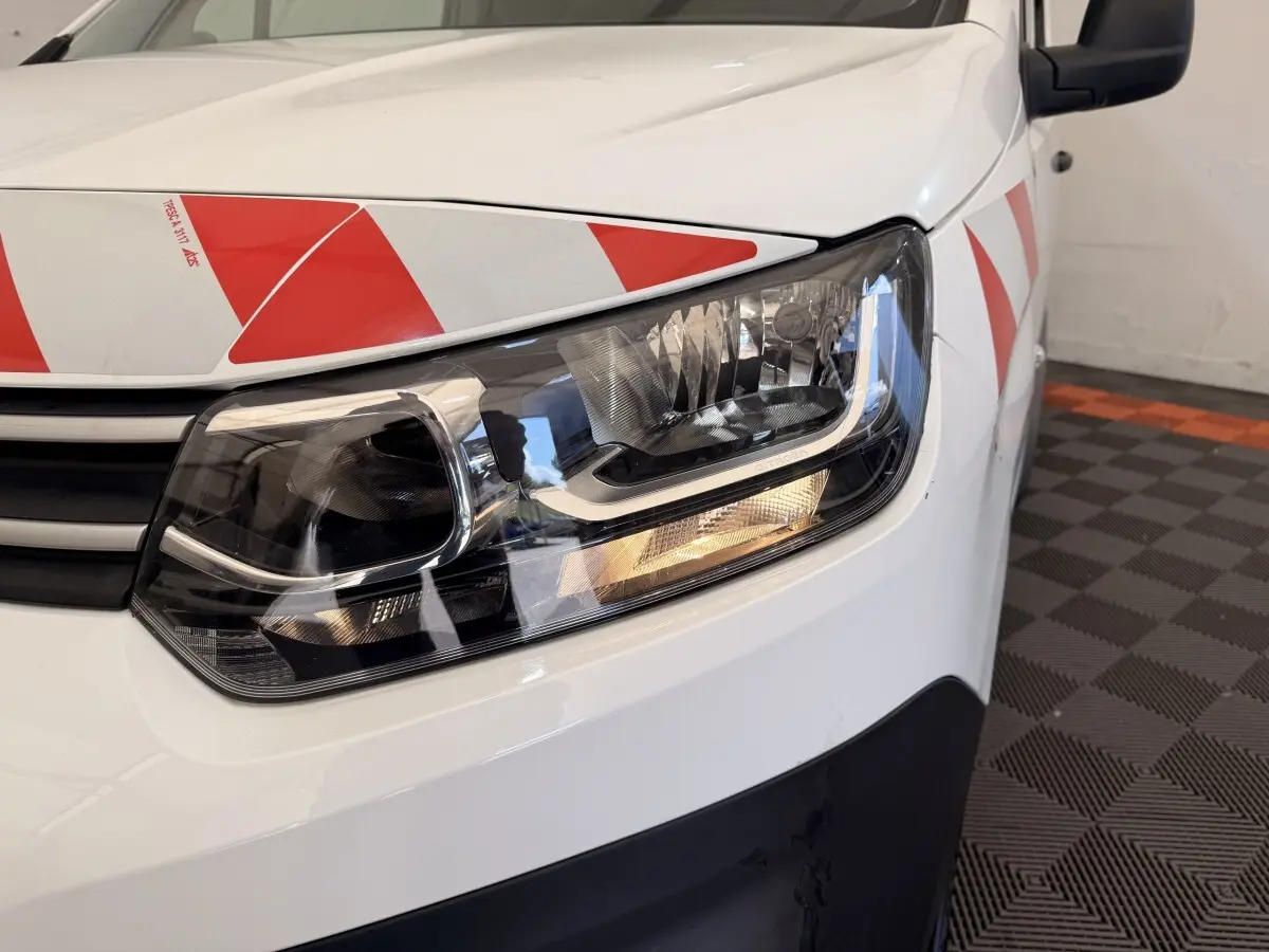 Gros plan sur l'avant droit blanc d'un Citroën Berlingo 2019 avec bandes rouges réfléchissantes sur le capot et la porte.
