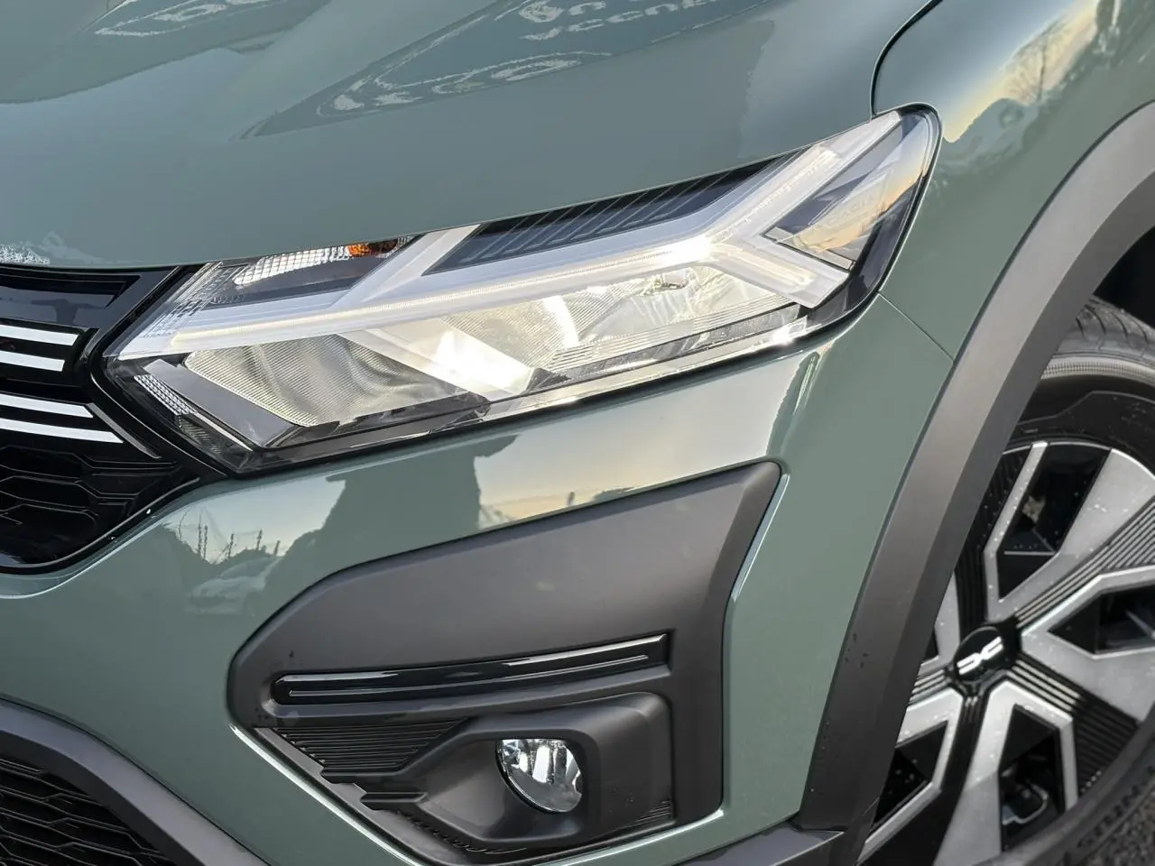 Gros plan sur l'avant droit du Dacia Sandero Stepway 2025 en kaki lichen, avec phares LED et enjoliveur de roue noir et argent.