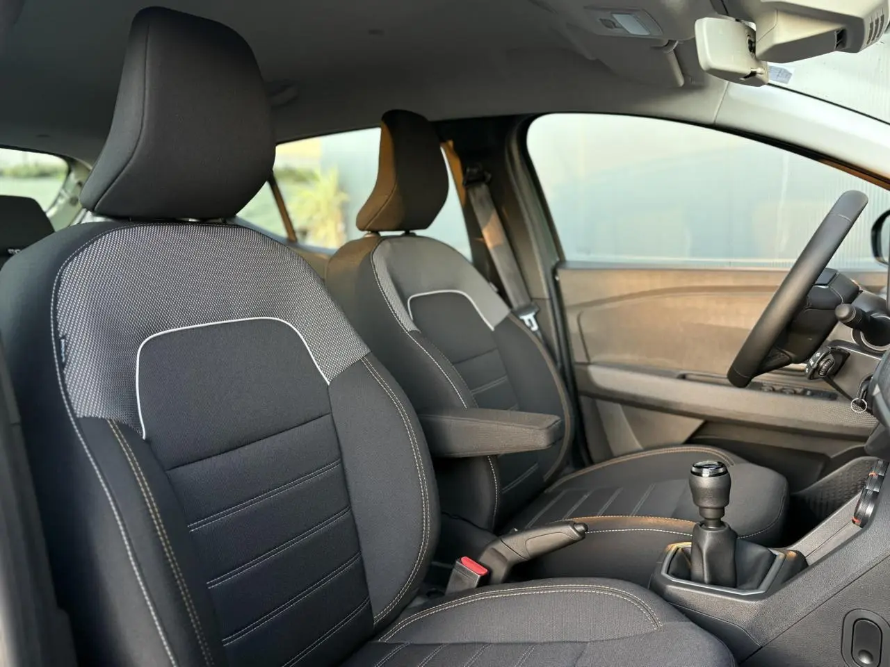 Vue intérieure côté conducteur de la Dacia Sandero Stepway 2025 avec sièges noirs et accoudoir central.