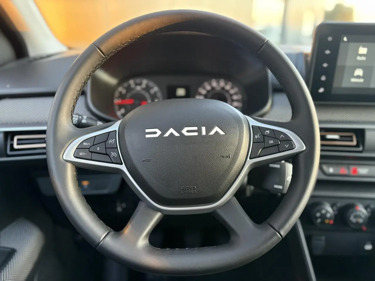 Volant noir en cuir avec logo Dacia au centre, tableau de bord et écran tactile du Dacia Sandero Stepway 2025 visibles en arrière-plan