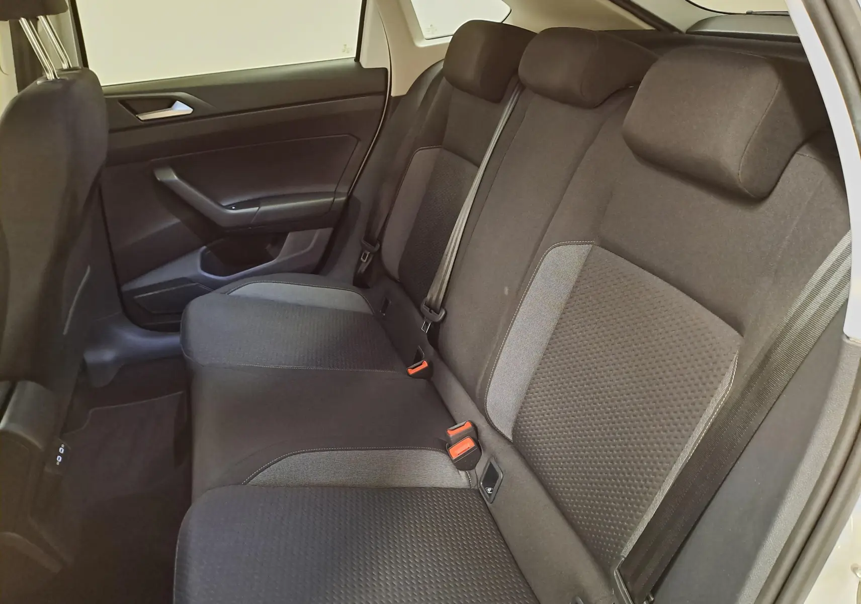 Vue intérieure côté droit des sièges arrière noirs du Volkswagen Taigo 2024, avec ceinture de sécurité et habillage de porte sombre.