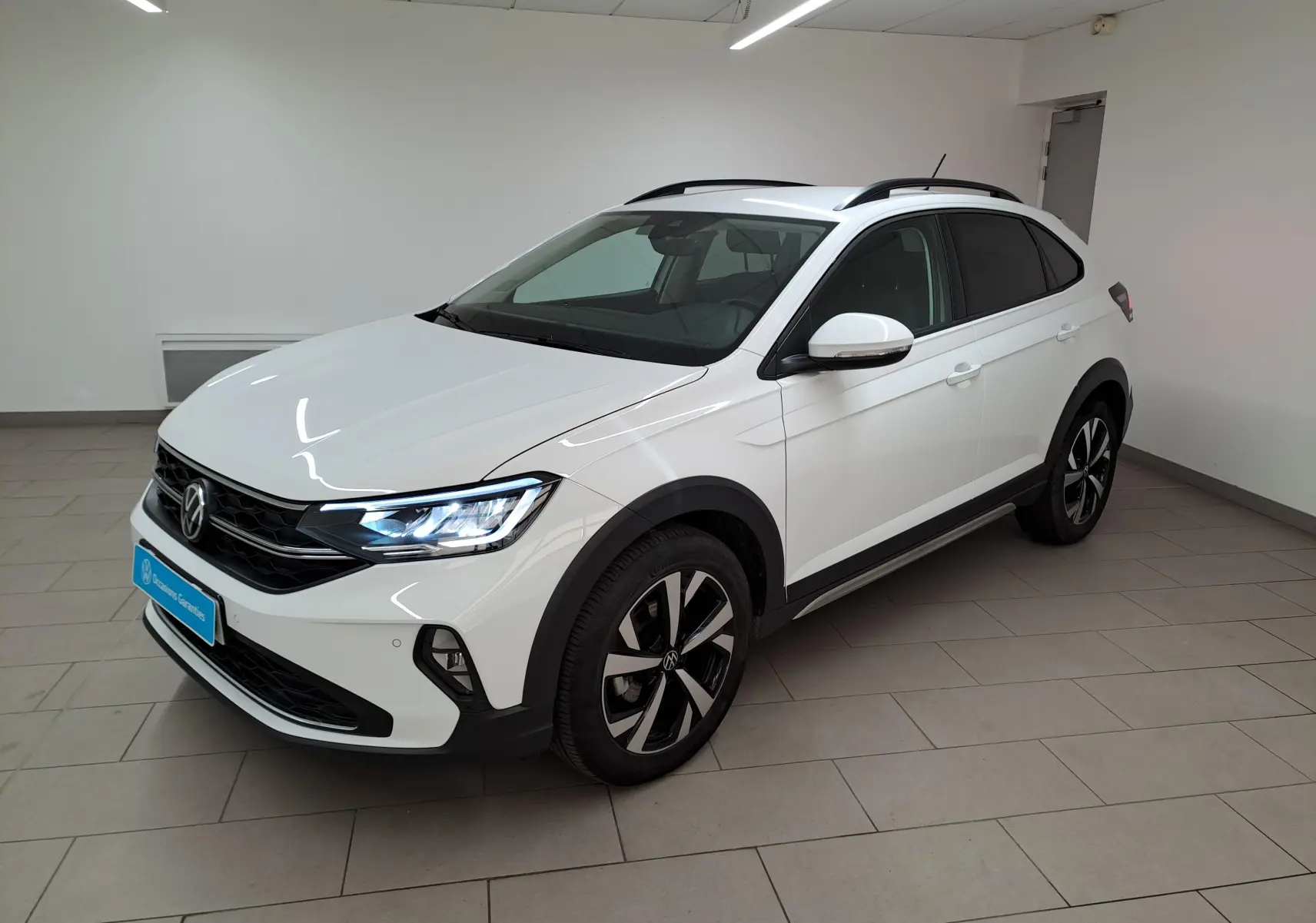 Volkswagen Taigo blanc pur en vue 3/4 avant droit, avec jantes alliage noires et projecteurs LED allumés.