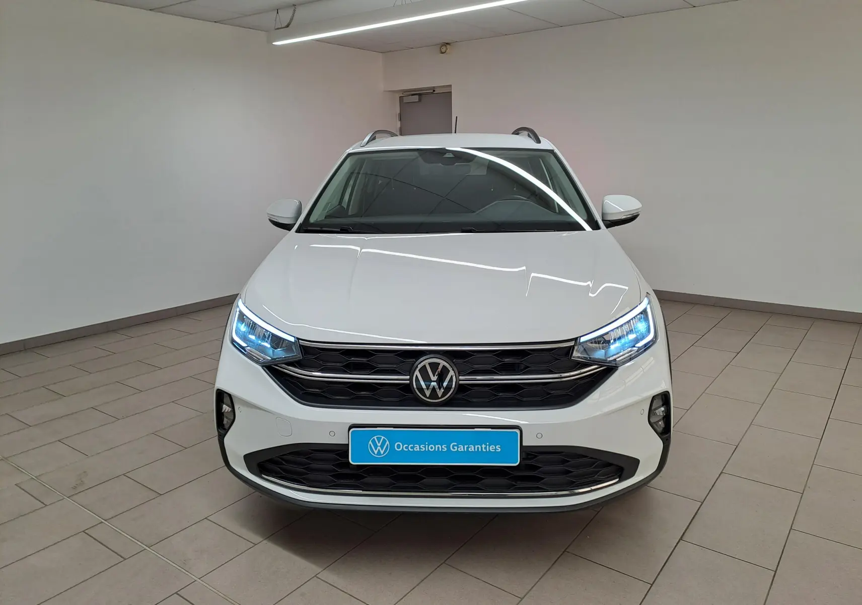 Volkswagen Taigo blanc pur vu de face, avec projecteurs LED allumés et calandre noire distinctive.