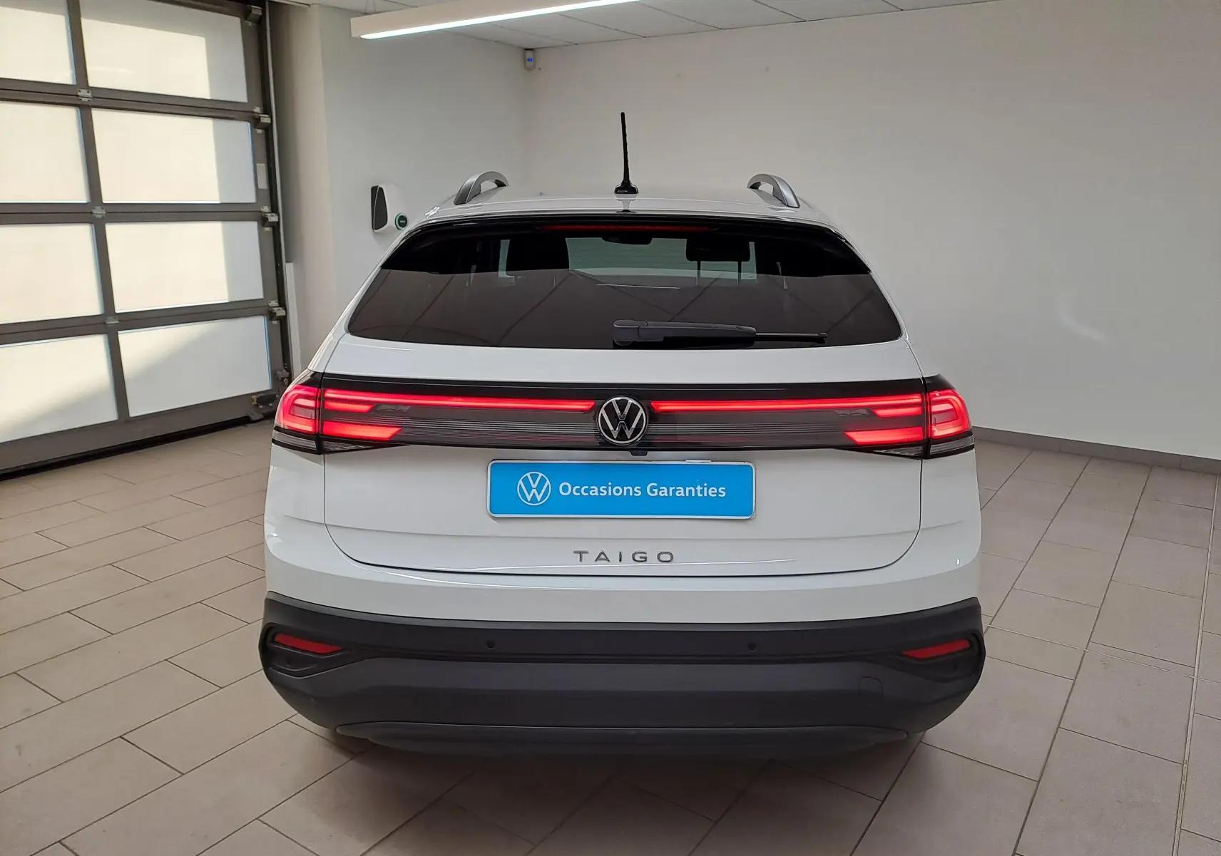 Vue arrière d'un Volkswagen Taigo blanc pur 2024 avec feux arrière allumés et logo VW visible.