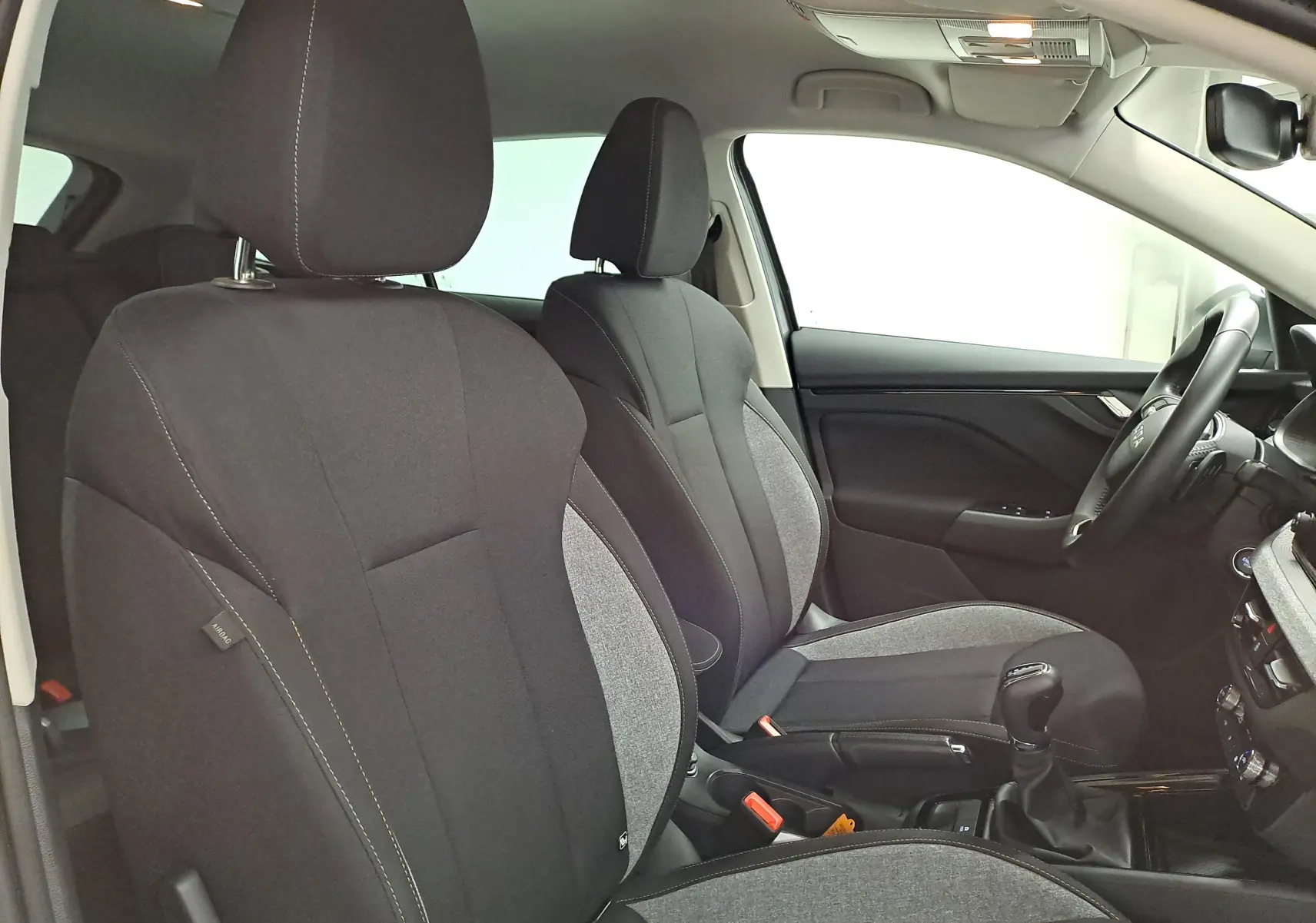 Vue intérieure côté droit des sièges avant en tissu gris et noir d'une Skoda Scala 2025 avec volant et levier de vitesse visibles.