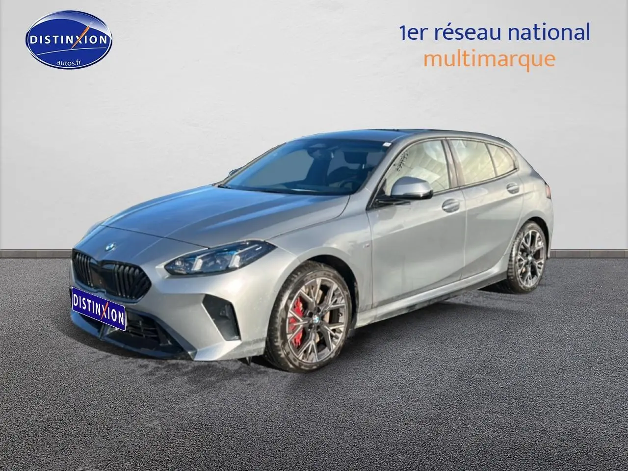 BMW Série 1 118da gris skyscraper vue 3/4 avant droit avec jantes 18 pouces bicolores et étriers rouges.