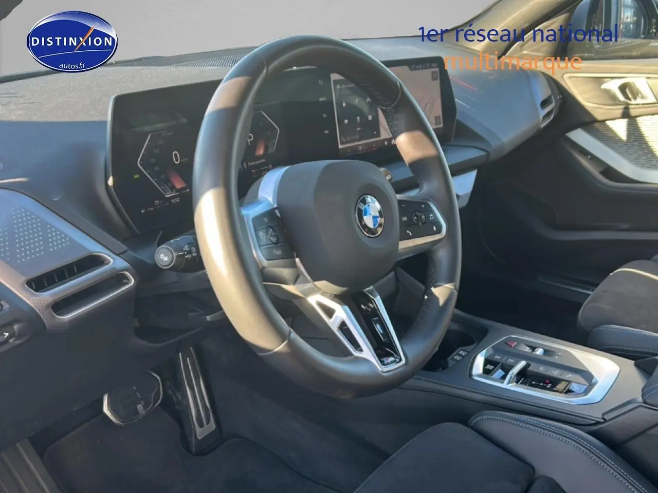 Vue intérieure côté conducteur du tableau de bord et volant de la BMW Série 1 118da 2025 en tissu noir avec coutures bleues.