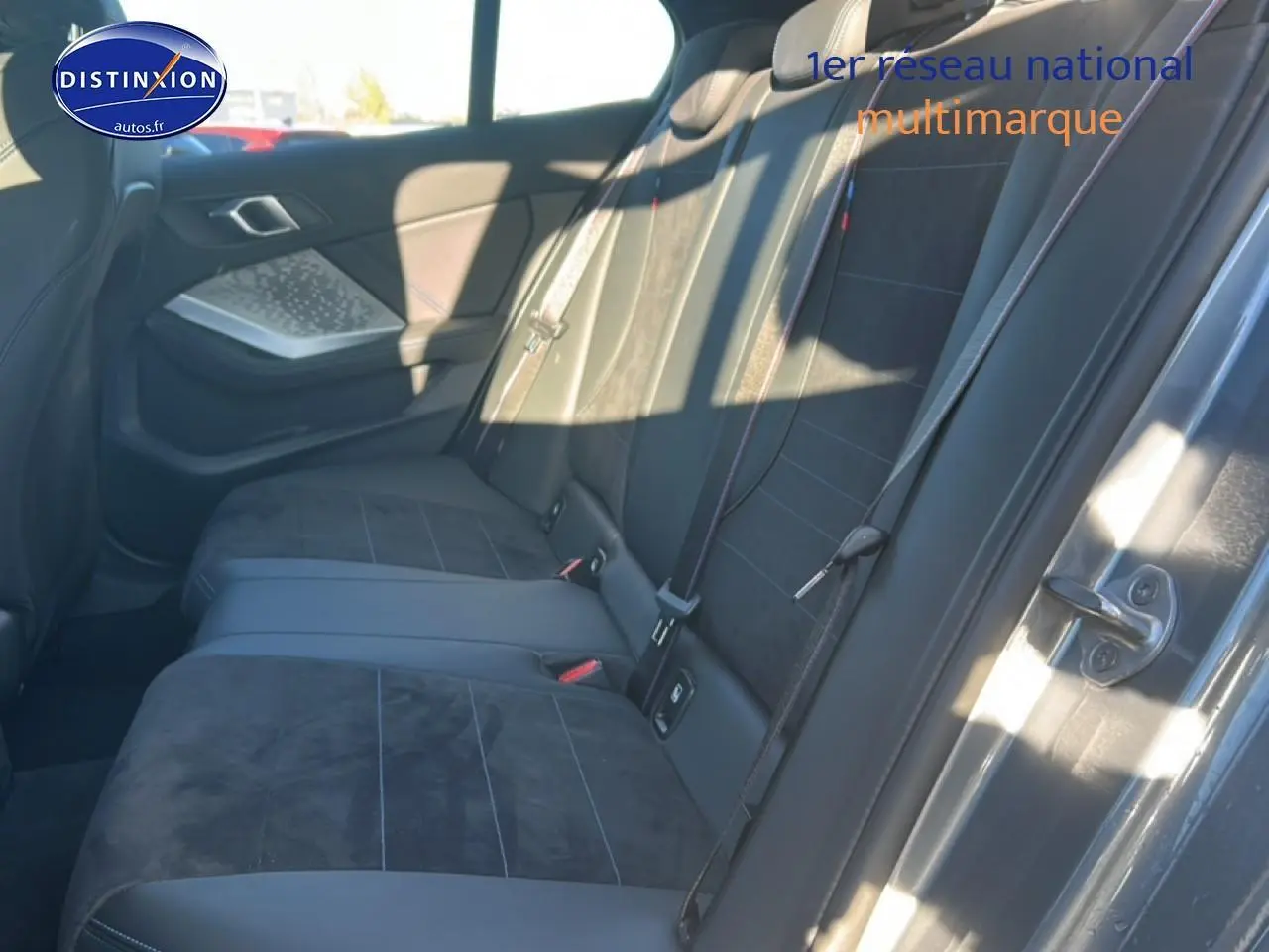 Vue latérale droite de l’arrière intérieur de la BMW Série 1 118da 2025 avec sièges en alcantara noir et coutures bleues.