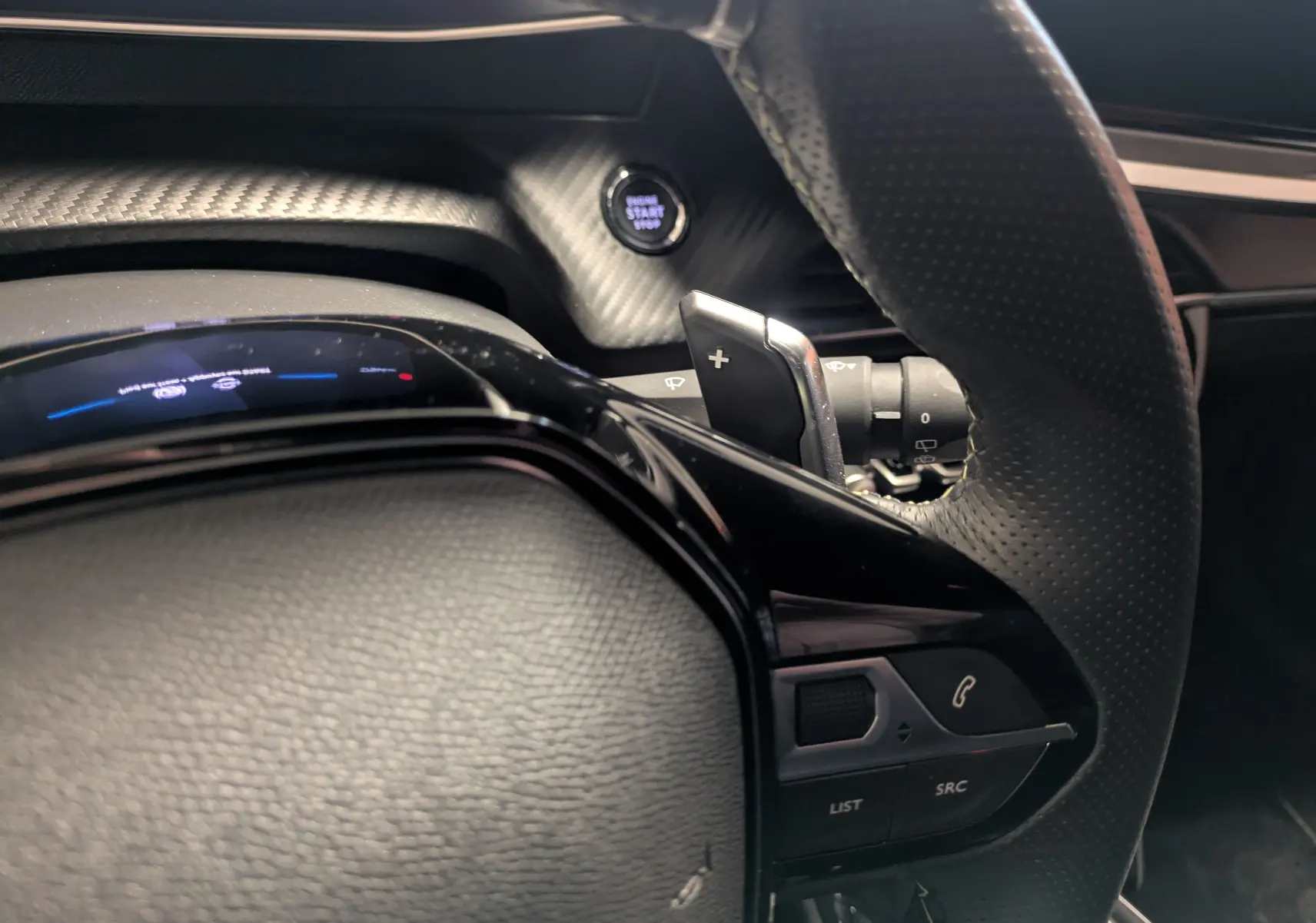 Gros plan sur le volant perforé et les commandes multifonctions du Peugeot 2008 Hybrid 145 e-DCS6 GT, intérieur noir.