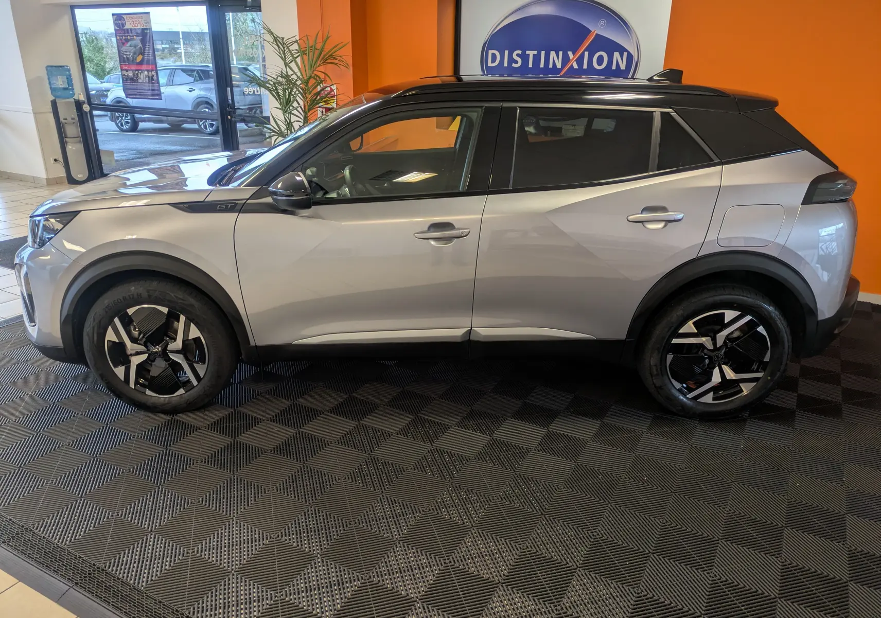 Profil côté gauche du Peugeot 2008 Hybrid 145 e-DCS6 GT 2025 en gris Artense avec toit noir, présenté en intérieur showroom.